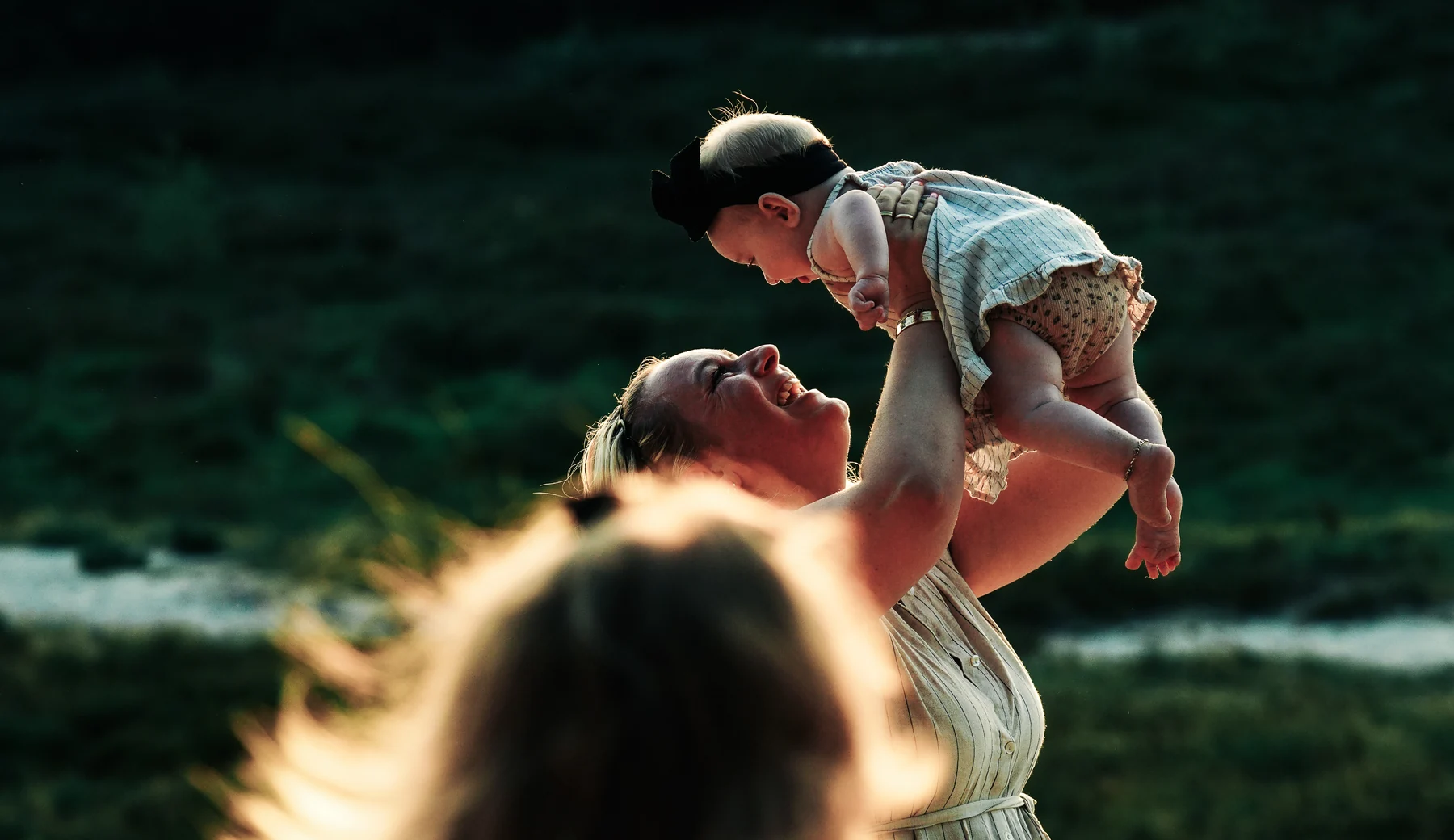 Een moeder tilt haar baby lachend in het avondlicht