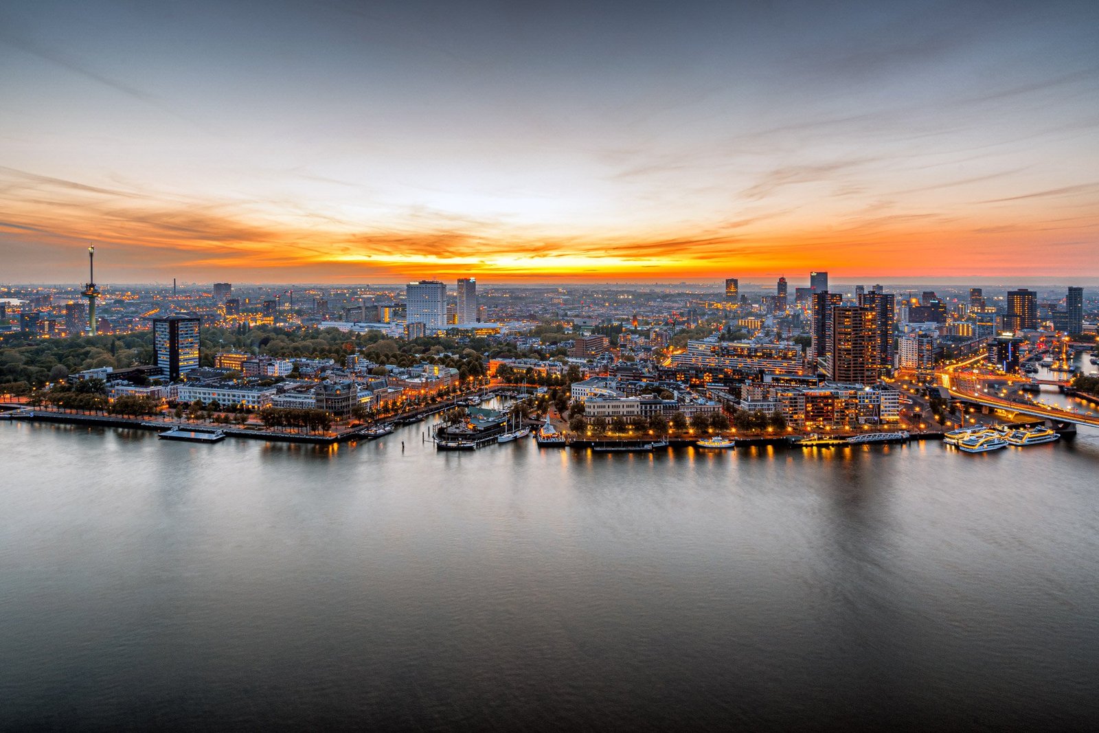 Uitzicht over Rotterdam bij zonsondergang, met lichtjes langs het water