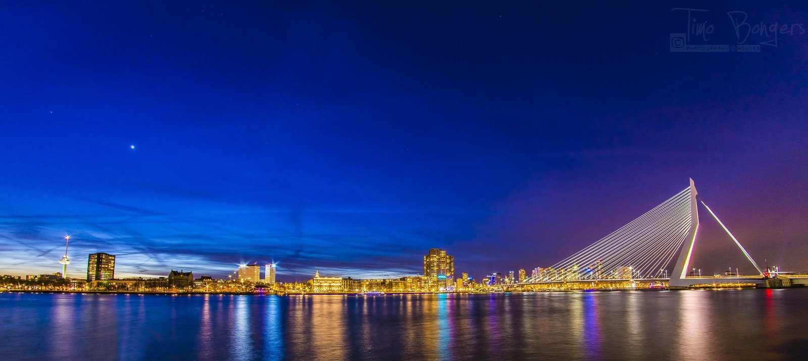 Erasmusbrug verlicht in het blauwe uur vanaf de waterkant
